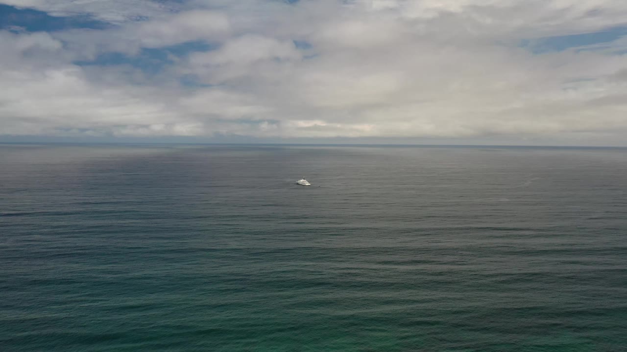 Los Cabos open water remains wide in frame, with darker ripples in the foreground, a small white horizon object, and no visible people.
