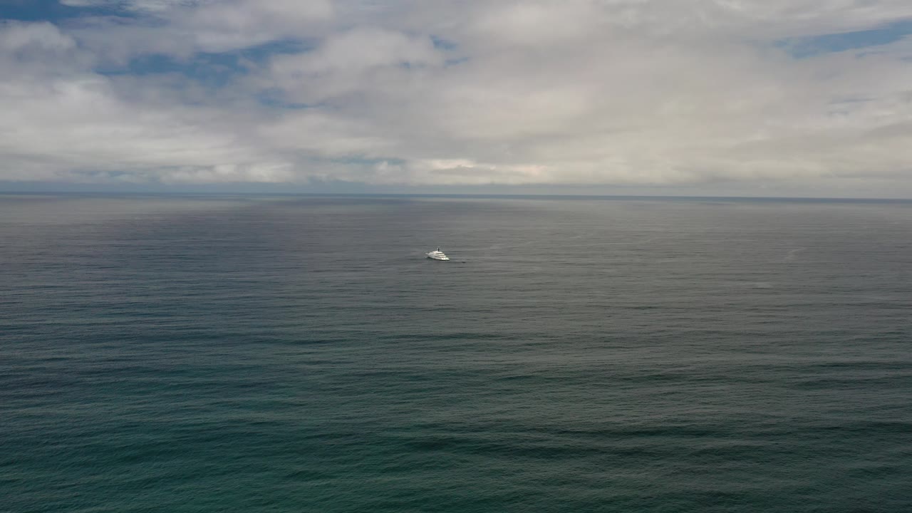 Wide Los Cabos ocean view at the start of the clip, with blue-green water, a level horizon, layered gray clouds, and no visible people.