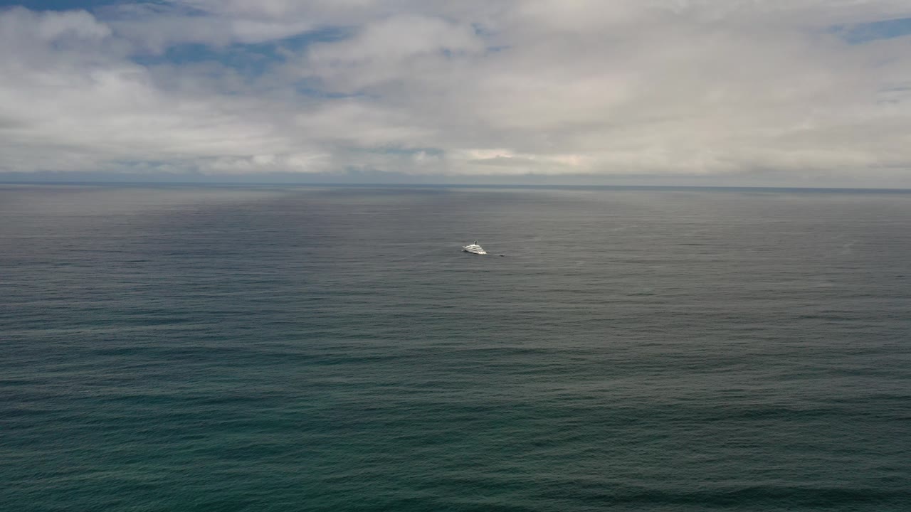Wide Los Cabos ocean view at the start of the clip, with dark water, a low cloudy horizon, a small white boat left of center, and no visible people.