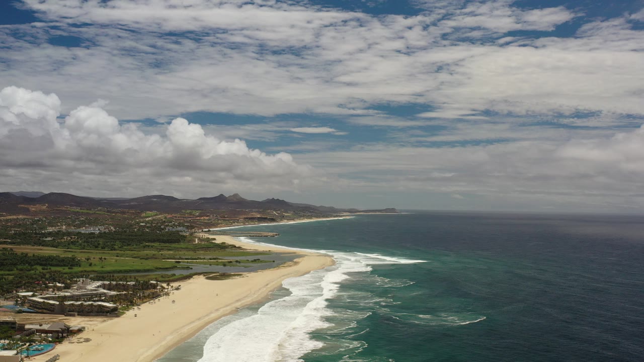 Aerial view of sandy beach, surf, ocean, inland town, and hills