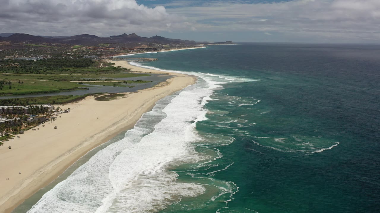 Aerial view of sandy shoreline with white surf and dark blue ocean.