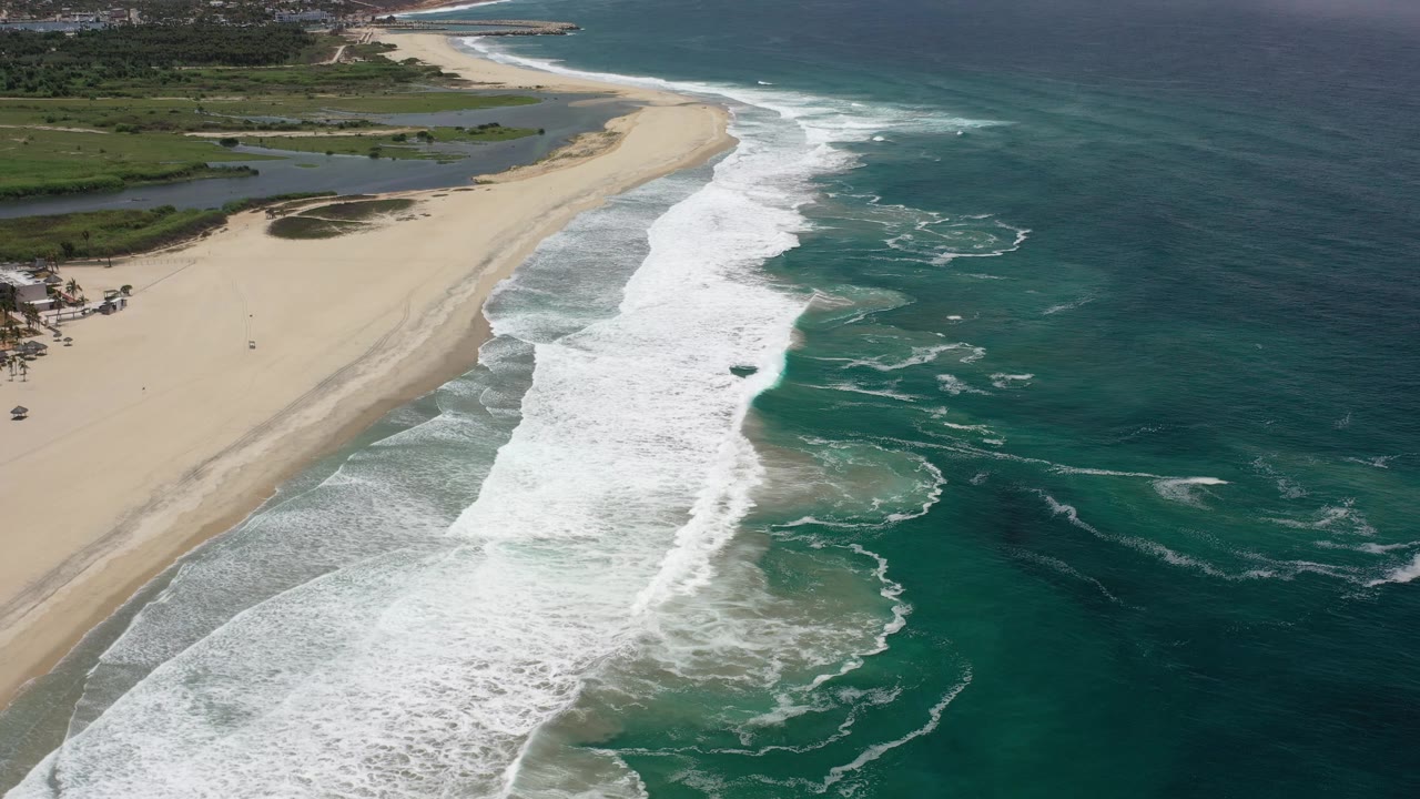 White waves curl toward a sandy point with blue ocean offshore.