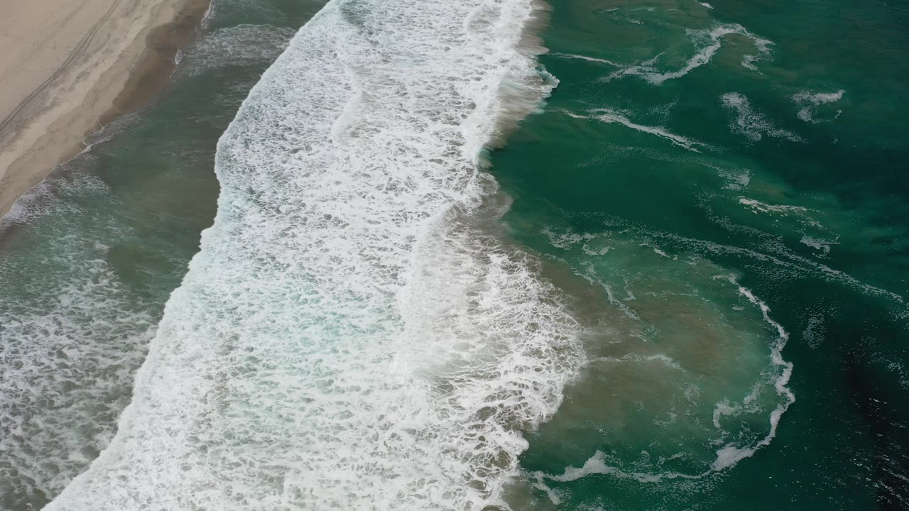 Diagonal wave break separates sandy shoreline from darker water.