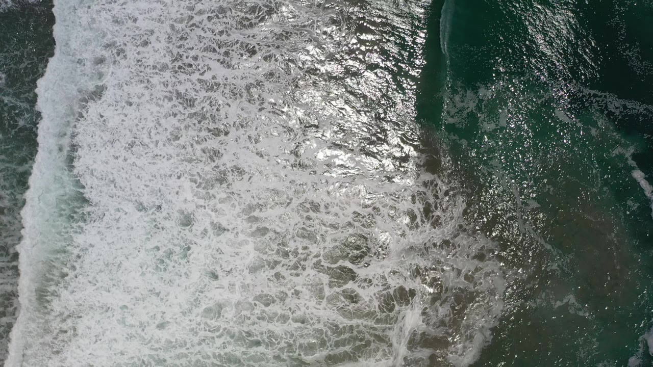 Bright surf wash spreading across darker ocean