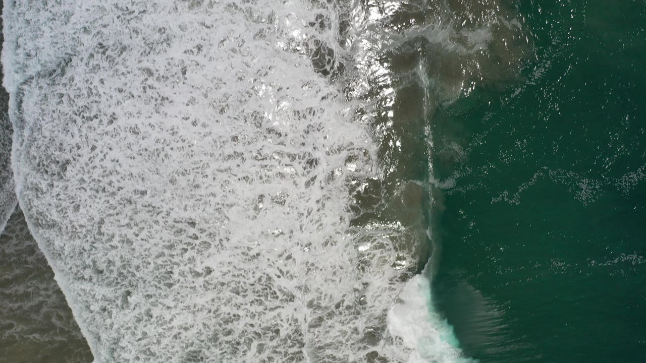 Top-down view of white surf foam meeting turquoise green water in Los Cabos, Mexico, with no visible people.