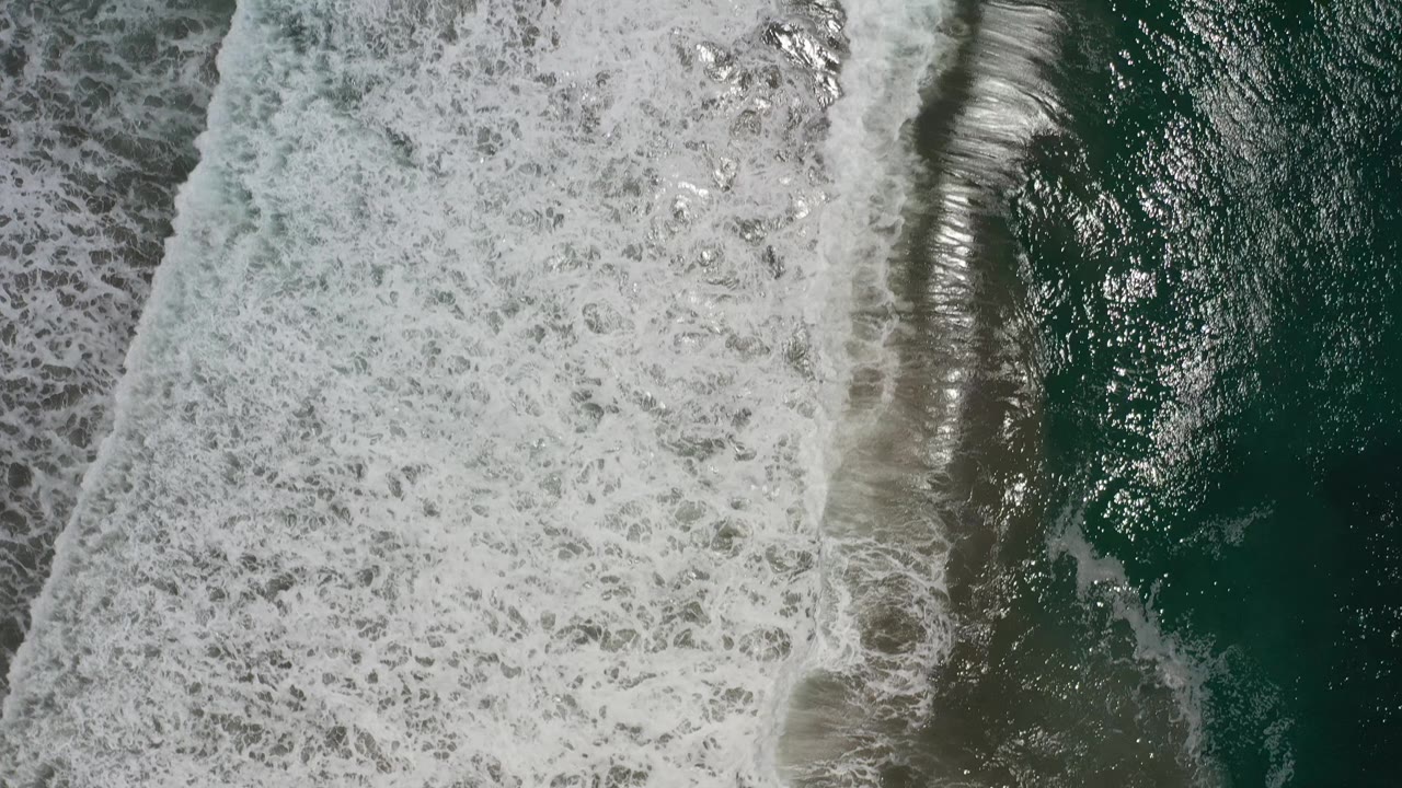 A dense band of white wave foam runs beside darker green ocean water in Los Cabos, Mexico, with no visible people.