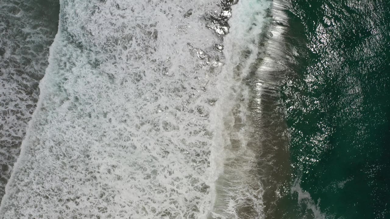 Foamy tide line and reflective green water from above.