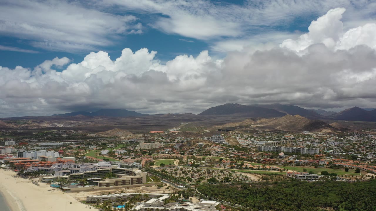 Wide aerial view of a city valley beneath large white clouds.