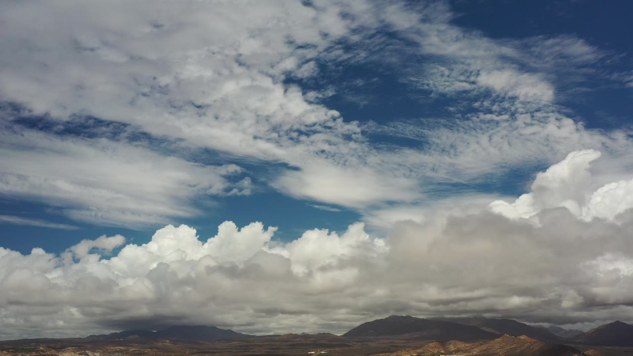 Opening frame of Los Cabos, Mexico landscape with a low dark hill line beneath broad blue sky and dense white clouds, no visible people.