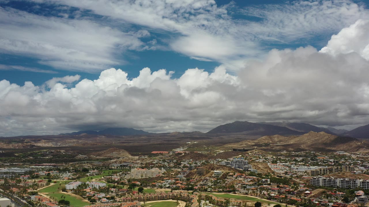 Aerial view of city blocks below dry hills and large clouds.