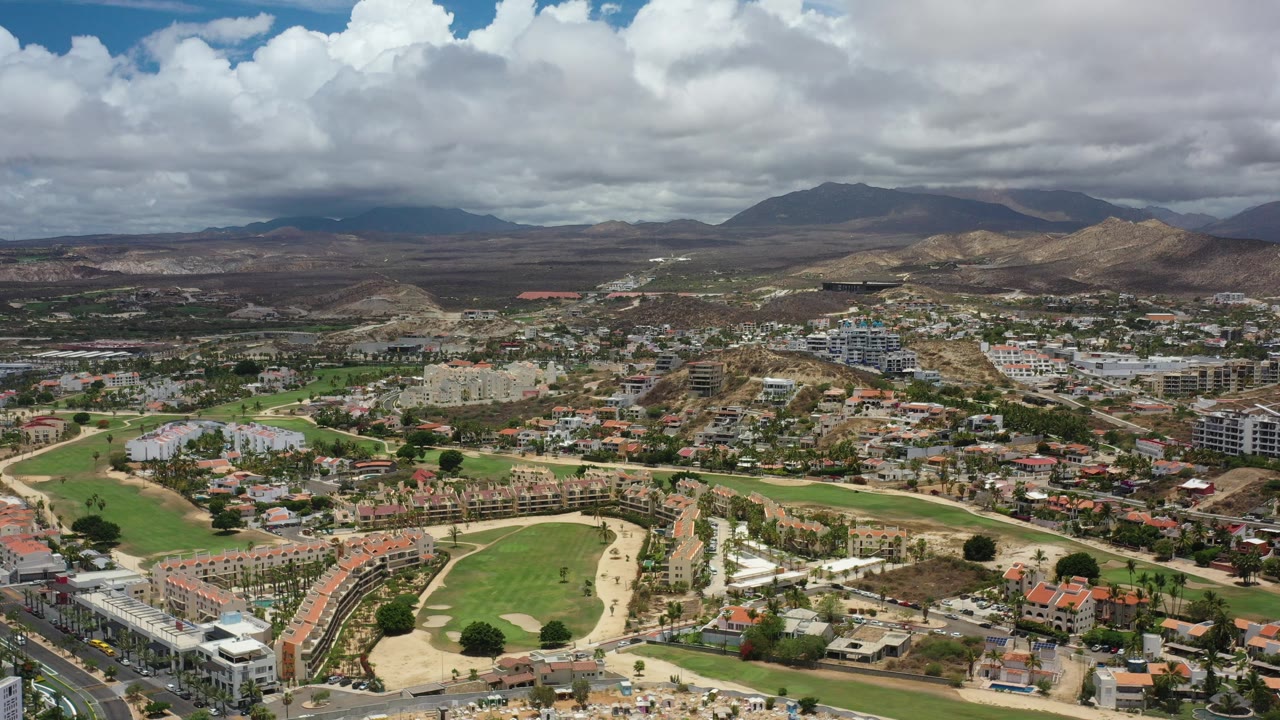 Aerial view of golf course, homes, roads, hills, and cloudy mountains.