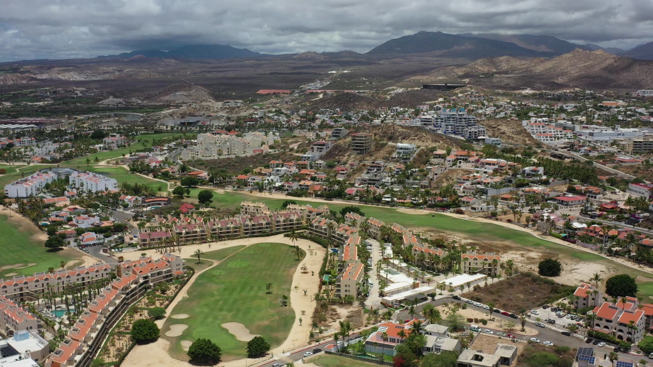 Aerial view of golf fairways, homes, and mountains under clouds.