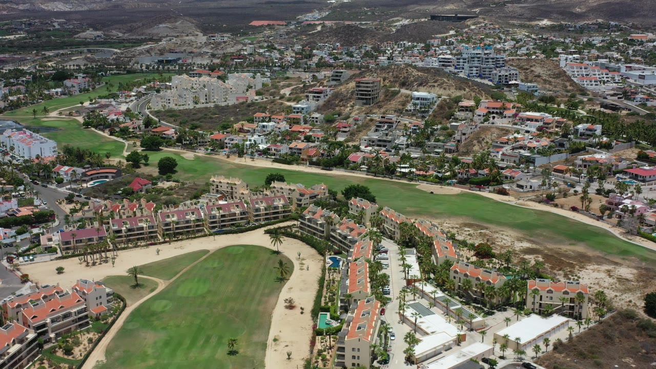 Elevated view of golf greens, tan paths, villas, roads, and low mountains.