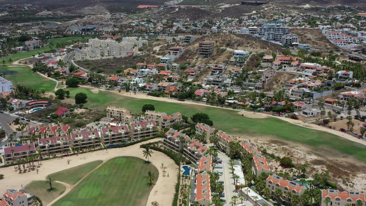 Aerial view of golf greens, red-roofed homes, roads, and dry hills.