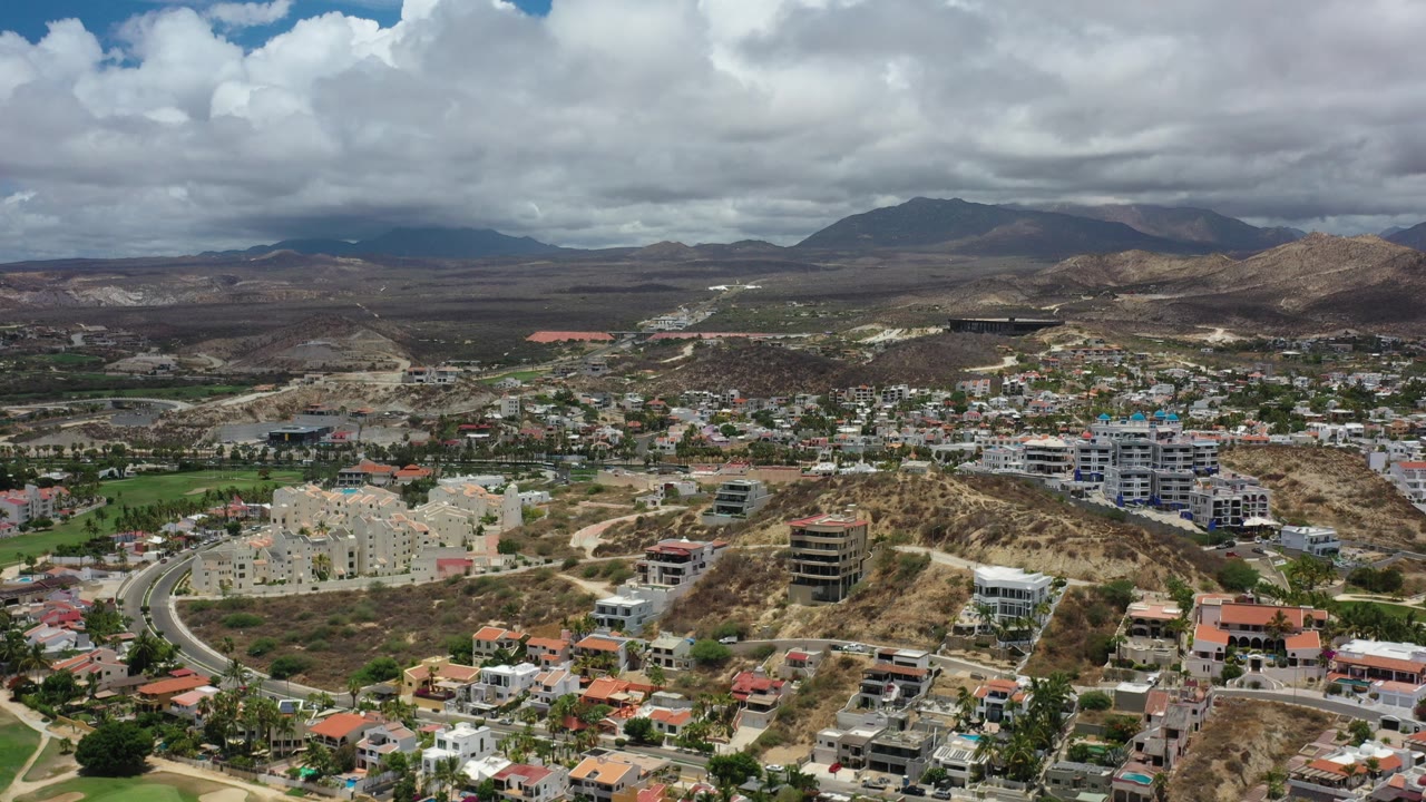 Aerial view of hillside homes and roads below cloudy mountains.