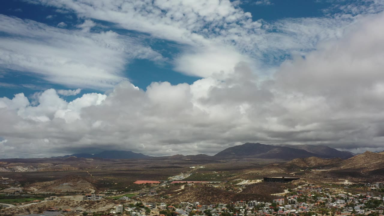 Mountain horizon under broad white clouds above a low city edge