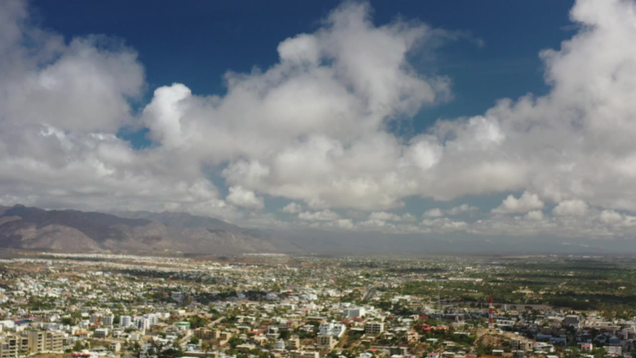 Wide aerial view of a populated valley under large white clouds.