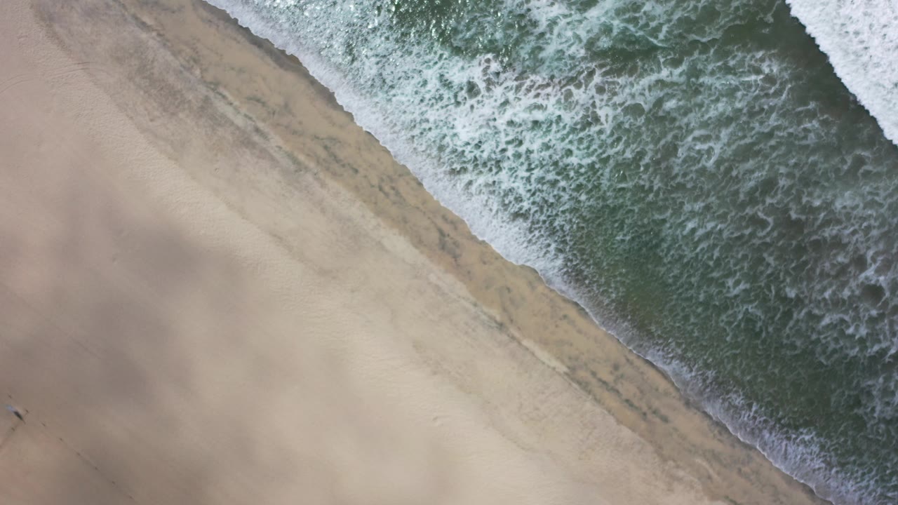 White wave edge crossing a sandy beach from above