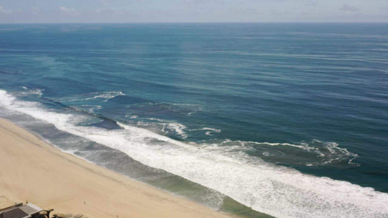 Empty beach and foamy surf seen from above with open ocean behind.