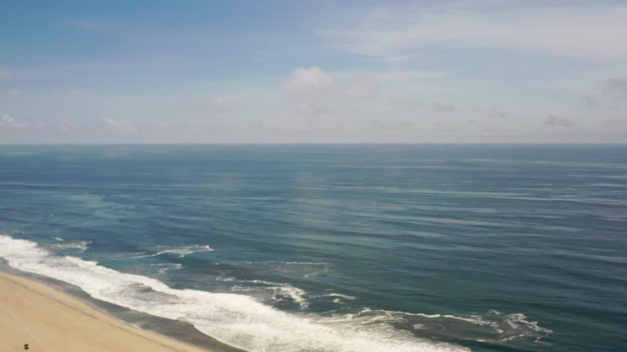 Beach edge, white surf, and textured ocean under light clouds.