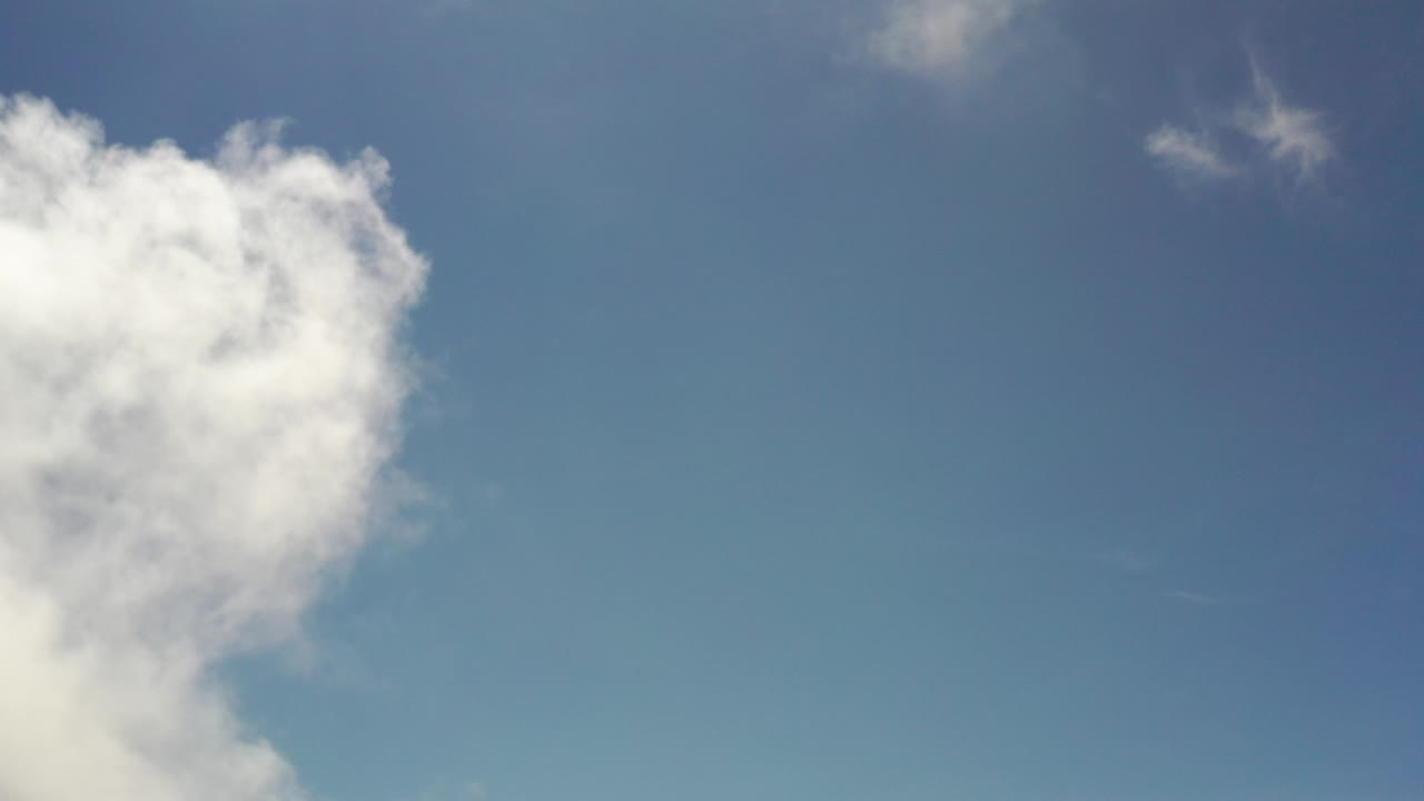 Los Cabos sky frame with a large white cloud entering from the left, open blue space across the right side, faint wisps near the top, and no visible people.