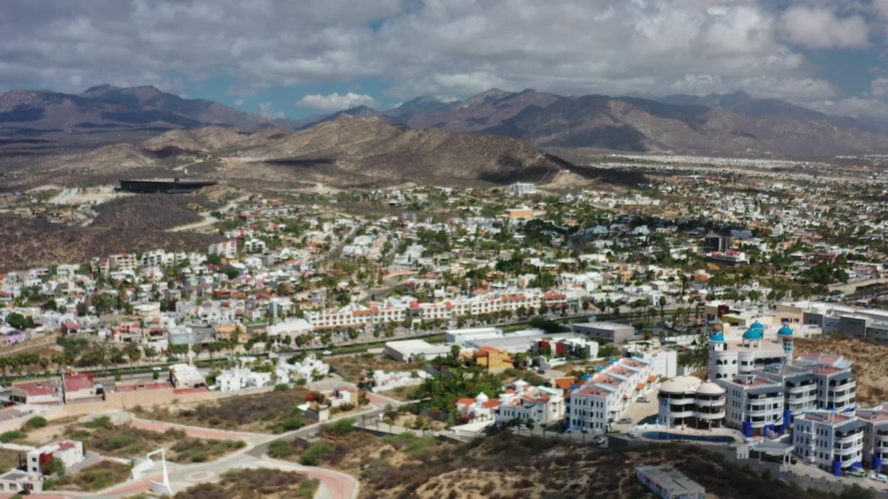 Aerial view of city buildings below dry mountains and clouds.