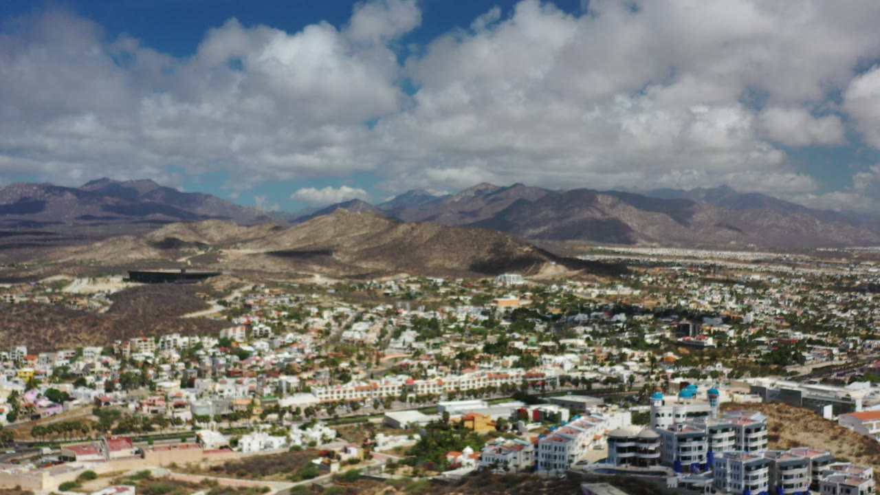 Aerial view of town buildings below dry hills and mountains under clouds.