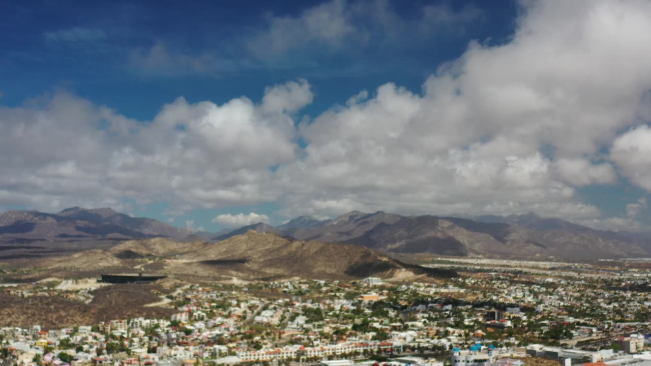 Low cityscape, desert hills, mountains, and thick clouds.