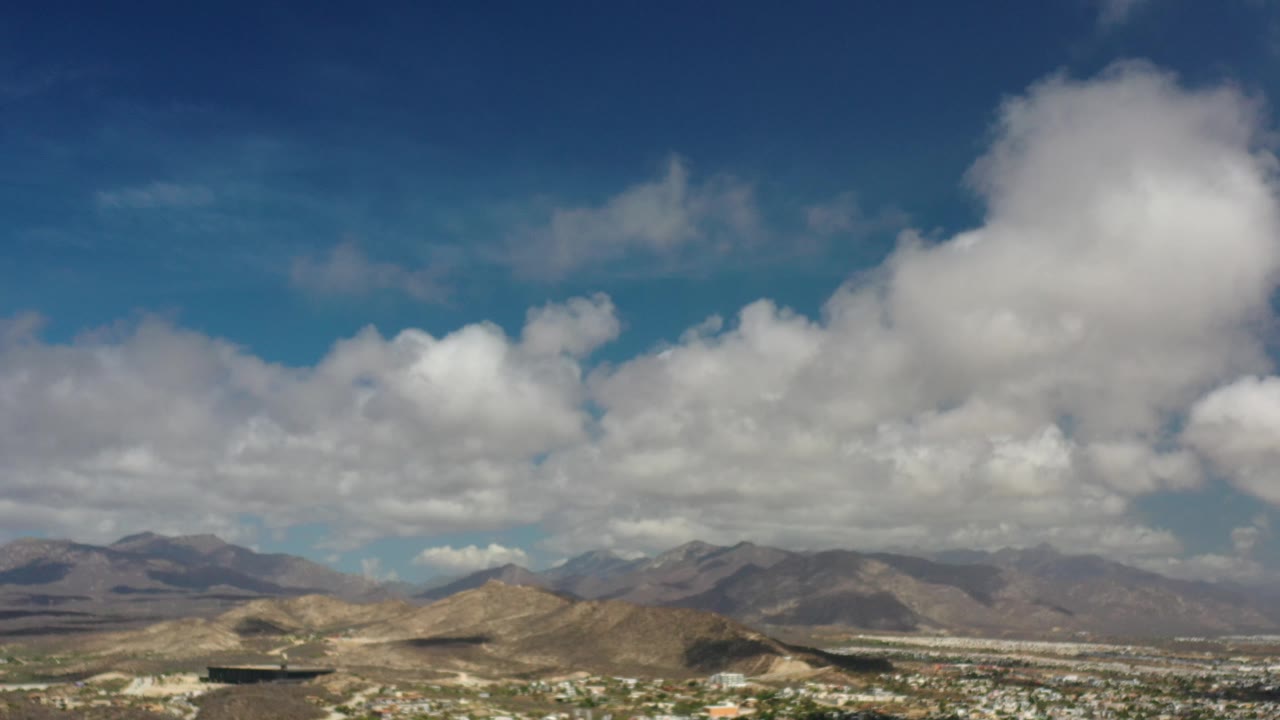 Cloud-filled sky over brown mountains and distant buildings.