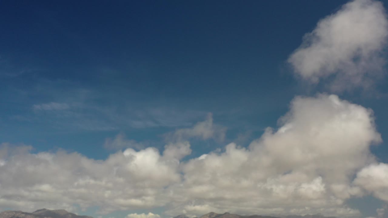 Opening frame of the Los Cabos clip with a deep blue sky, layered white clouds, faint land at the bottom edge, and no visible people.