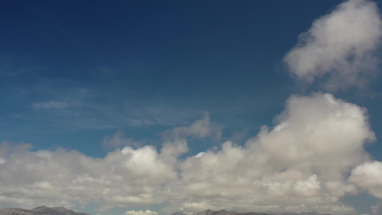 Los Cabos sky frame with bright cumulus clouds across the lower half, a taller cloud rising near the right side, and no visible people.