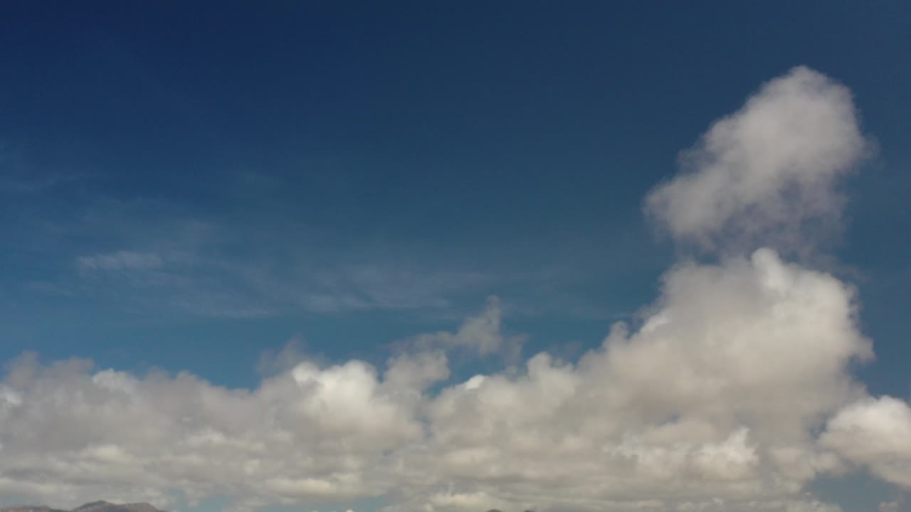 Blue sky with large white clouds above a low mountain horizon.