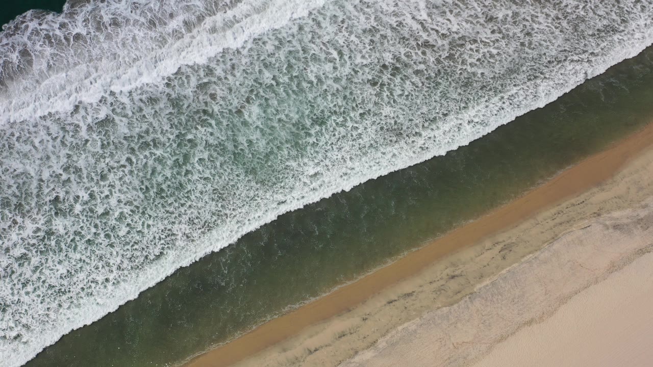 Overhead surf breaking diagonally onto sandy beach.