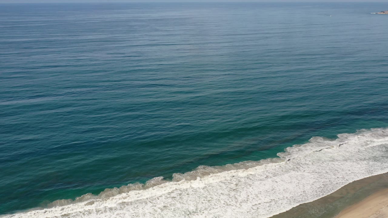 Empty shoreline with foamy waves and open ocean.