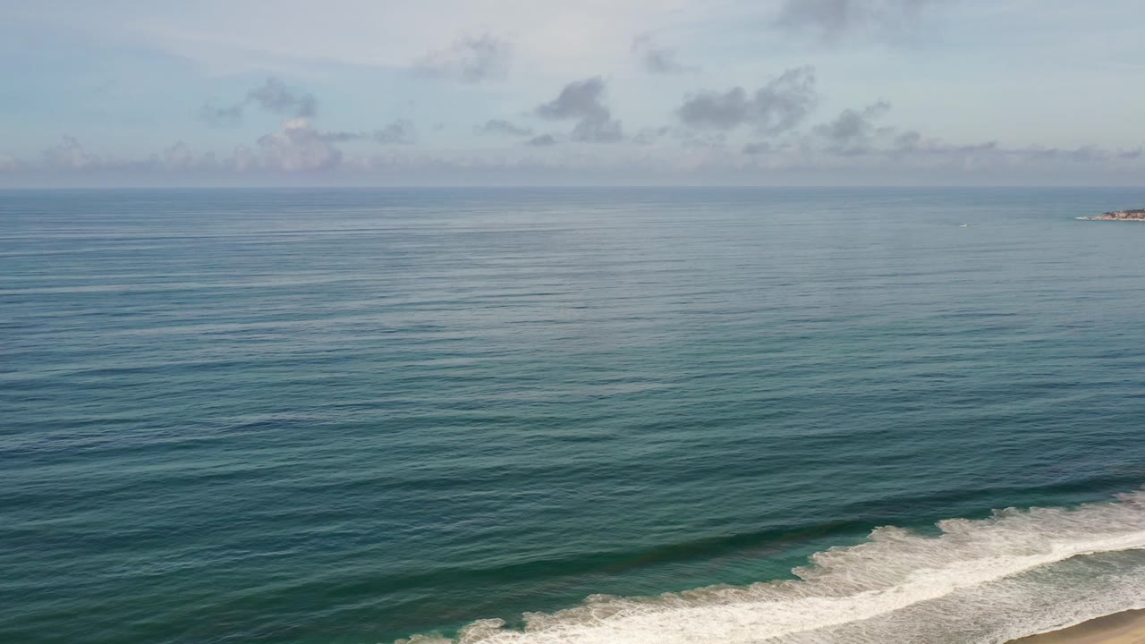 Ocean horizon with cloudy sky and surf curling along the beach edge.