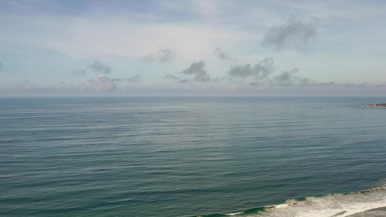 Los Cabos sea surface fills the frame beneath soft gray clouds, with a narrow band of white surf along the lower right and no visible people.