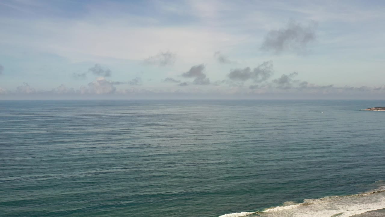 Open ocean with a distant rocky point and clouds across the horizon.