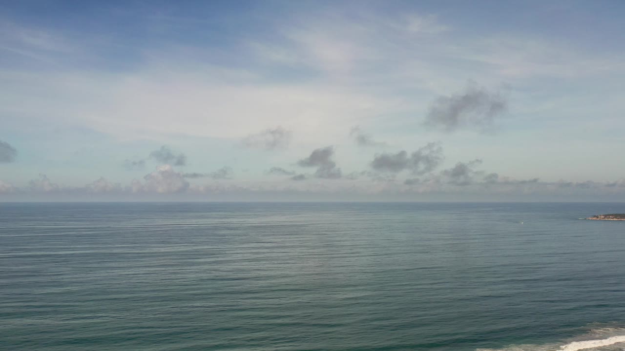 Open ocean and hazy cloud bands with distant rock at right