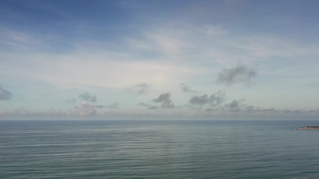 Los Cabos ocean frame with a small offshore landform near the horizon, soft cloud cover, and no visible people.