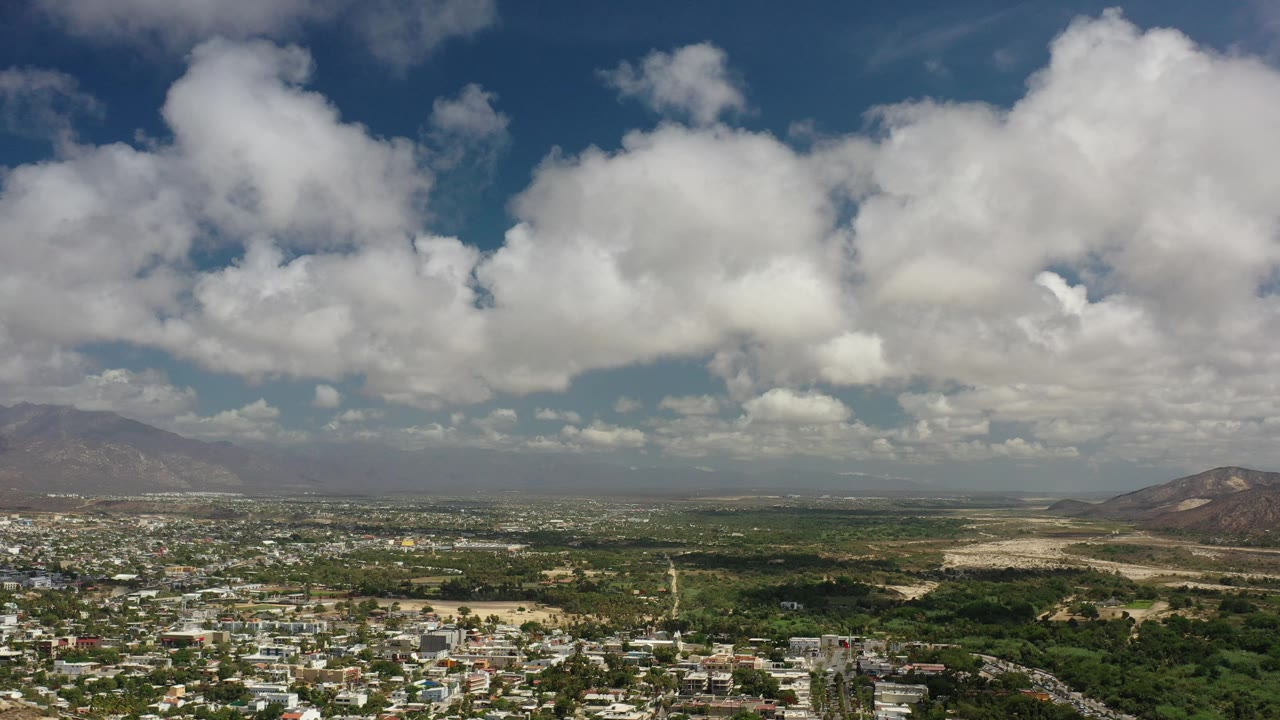 Wide aerial view of clouds over a mountain city landscape.