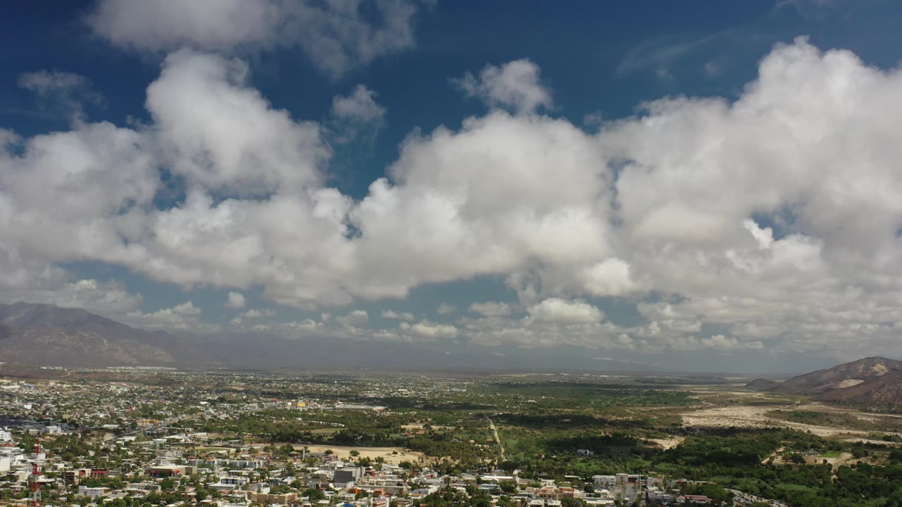 Cloud-filled sky above mountains, low buildings, and open land.