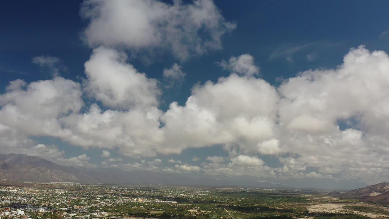 Wide aerial valley under large white clouds and blue sky.