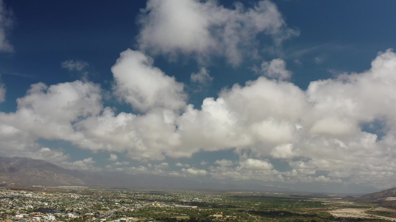 Large clouds stretching across blue sky over low town and hills