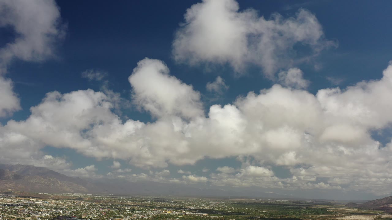 White clouds over blue sky and a distant desert landscape.
