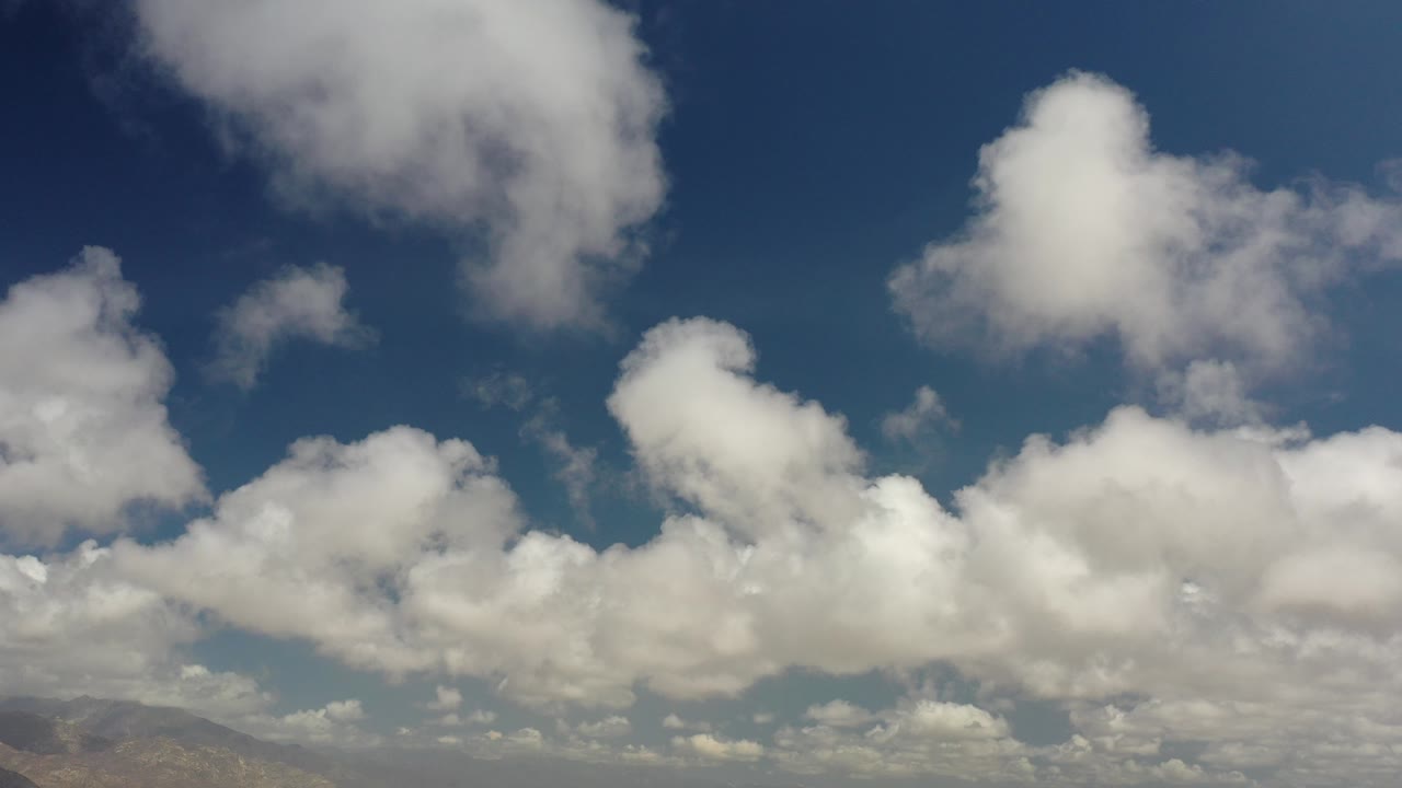 Opening frame of Los Cabos, Mexico sky footage with scattered white clouds, deep blue upper sky, a low distant horizon at the bottom, and no visible people.
