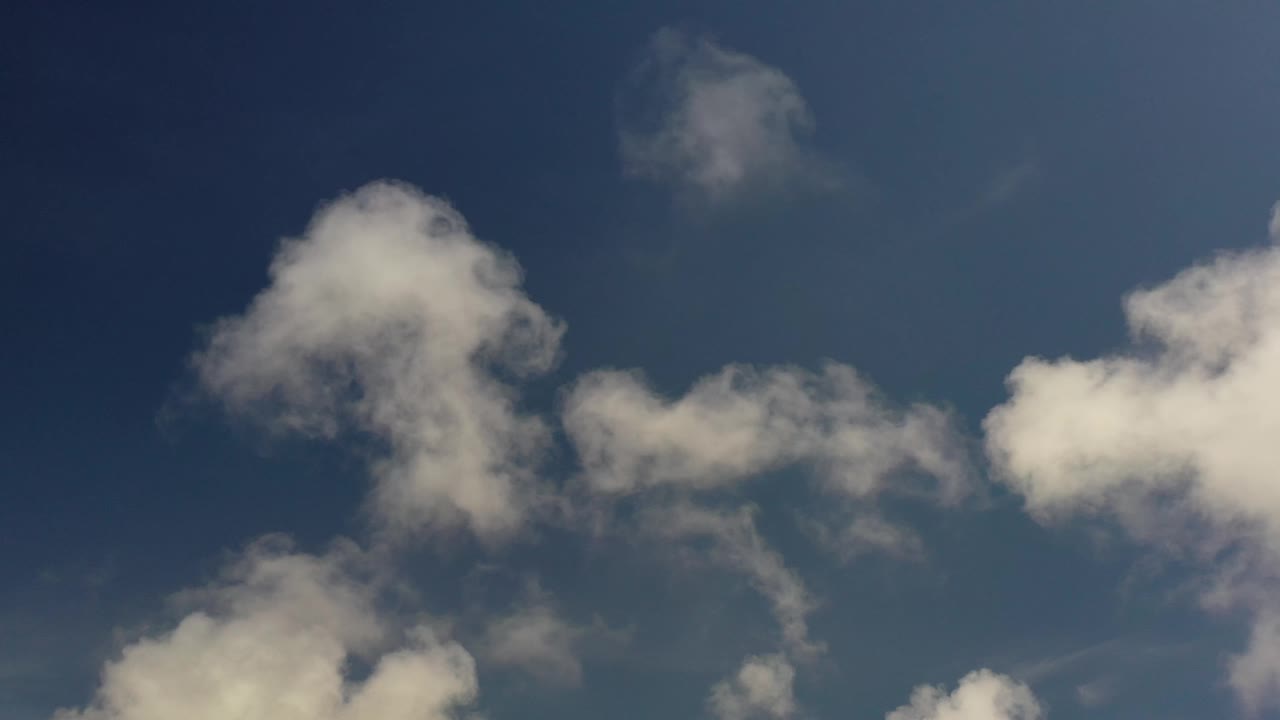 A large pale cloud cluster sits left of center in the Los Cabos sky, with smaller cloud bands to the right and no visible people.
