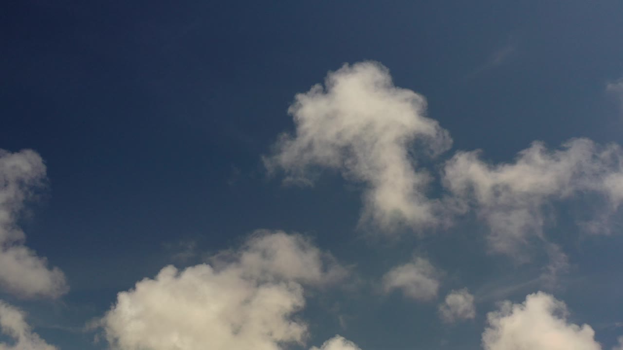 Early frame of a Los Cabos blue sky with a large soft cloud near the upper center, smaller clouds along the lower edge, and no visible people.