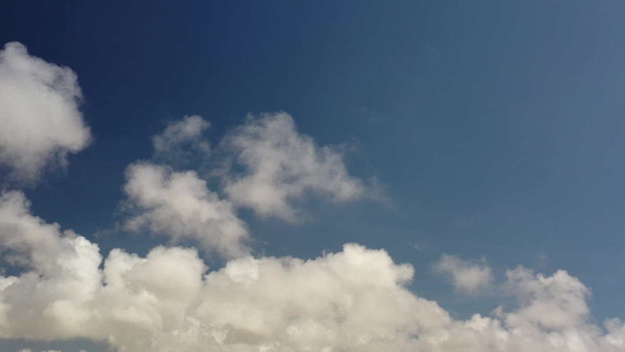 Opening frame of a Los Cabos, Mexico sky view with a dark blue upper sky, scattered white clouds below, and no visible people.