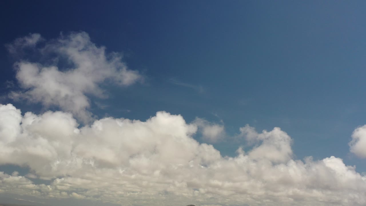 Opening frame of the Los Cabos, Mexico clip showing broad blue sky, layered white clouds, a thin distant mountain horizon, and no visible people.