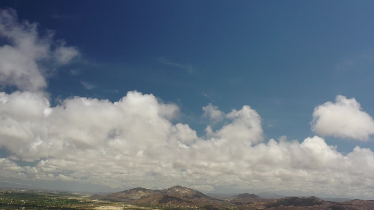 Wide mountain landscape under large white clouds and blue sky.